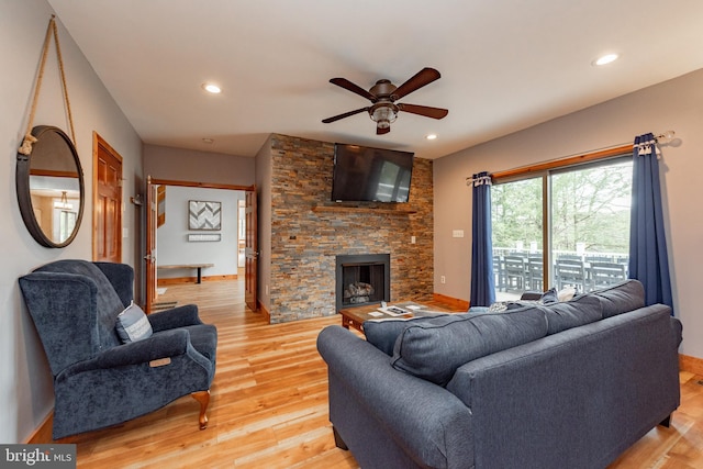 living room featuring light wood-type flooring, a stone fireplace, and ceiling fan