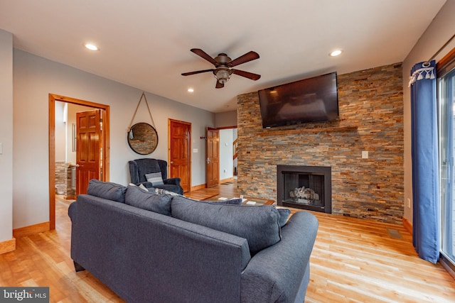 living room with ceiling fan, a stone fireplace, and wood-type flooring