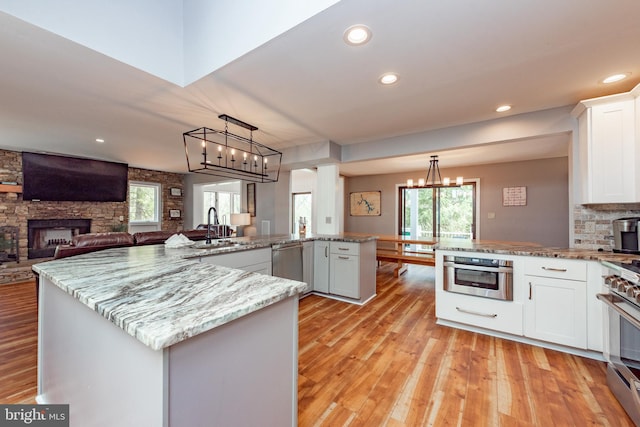 kitchen with sink, kitchen peninsula, pendant lighting, white cabinets, and appliances with stainless steel finishes