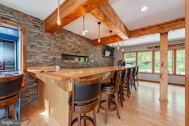 bar with pendant lighting, a stone fireplace, light wood-type flooring, beamed ceiling, and butcher block counters