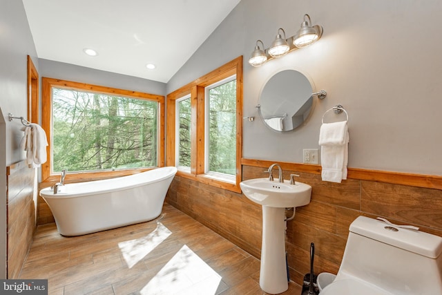 bathroom with lofted ceiling, toilet, a bathtub, tile walls, and hardwood / wood-style flooring