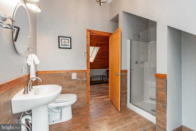 bathroom featuring wood-type flooring, toilet, tile walls, and a shower with shower door