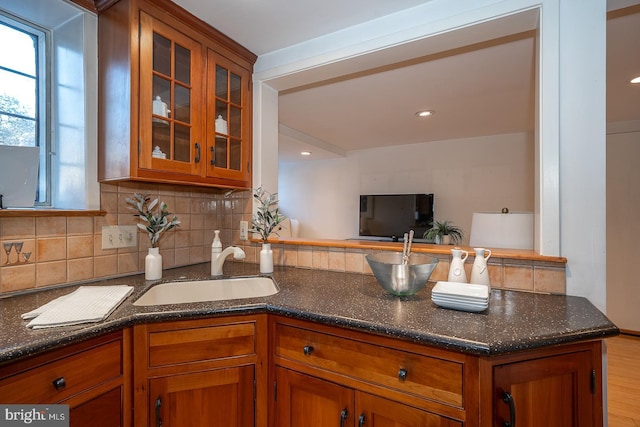 kitchen featuring sink, light wood-type flooring, dark stone countertops, kitchen peninsula, and backsplash