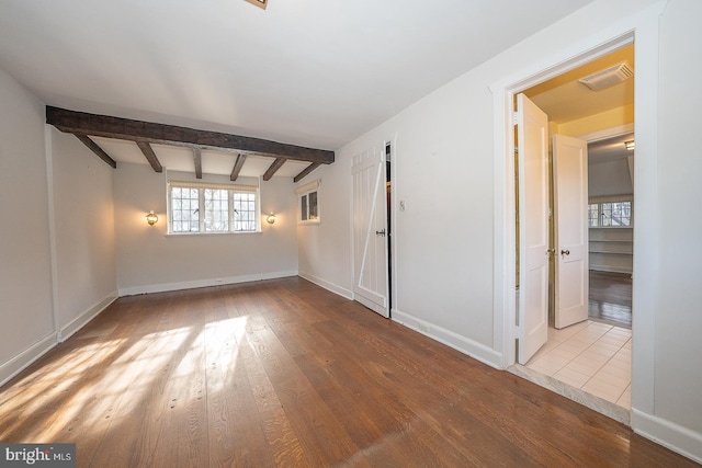 spare room featuring beamed ceiling and light hardwood / wood-style flooring