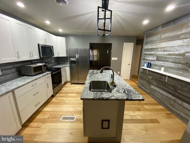 kitchen featuring stone counters, sink, an island with sink, and appliances with stainless steel finishes