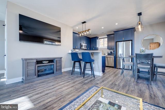 kitchen featuring dark wood-type flooring, a breakfast bar area, blue cabinetry, kitchen peninsula, and stainless steel appliances