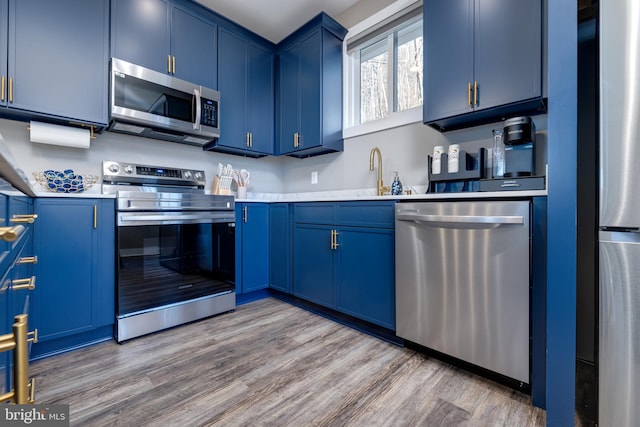 kitchen featuring hardwood / wood-style floors, sink, blue cabinetry, and appliances with stainless steel finishes