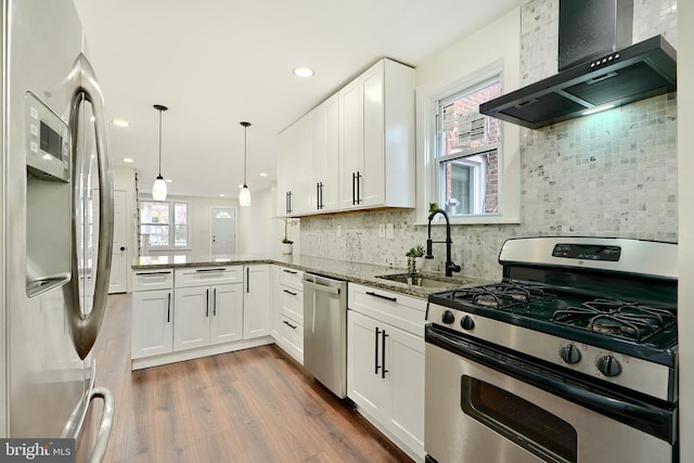 kitchen with sink, dark wood-type flooring, wall chimney range hood, white cabinets, and appliances with stainless steel finishes