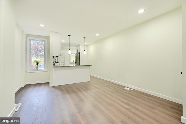 kitchen with white cabinets, dark hardwood / wood-style floors, stainless steel fridge, dark stone countertops, and decorative light fixtures