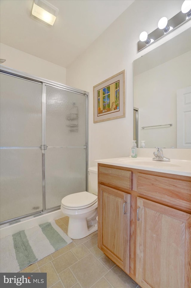 bathroom with tile patterned floors, vanity, a shower with shower door, and toilet