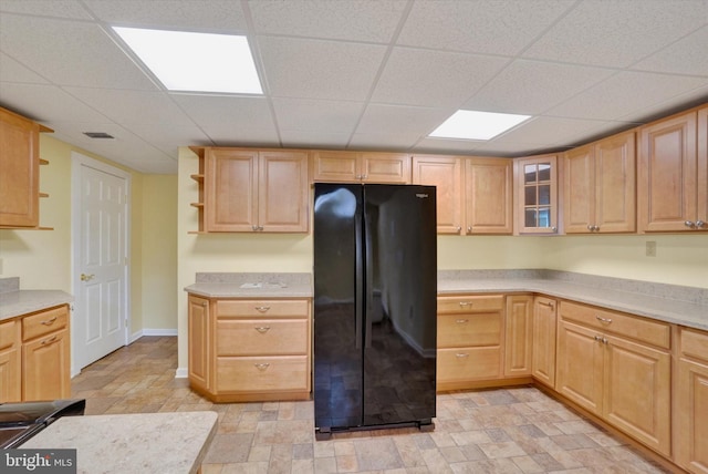 kitchen with a drop ceiling, black refrigerator, and light brown cabinets