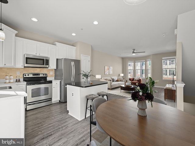 kitchen featuring white cabinetry, decorative light fixtures, a center island, appliances with stainless steel finishes, and backsplash