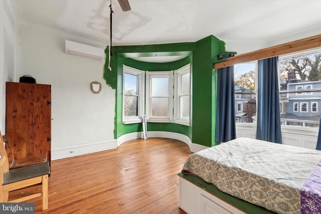 bedroom with light hardwood / wood-style floors, a wall unit AC, multiple windows, and ceiling fan