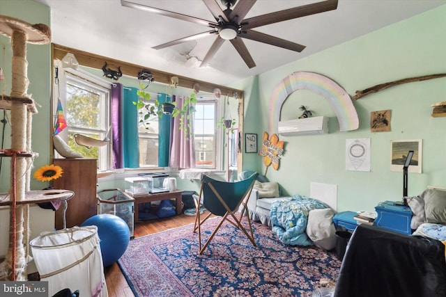 sitting room with a wall unit AC, ceiling fan, hardwood / wood-style floors, and a healthy amount of sunlight