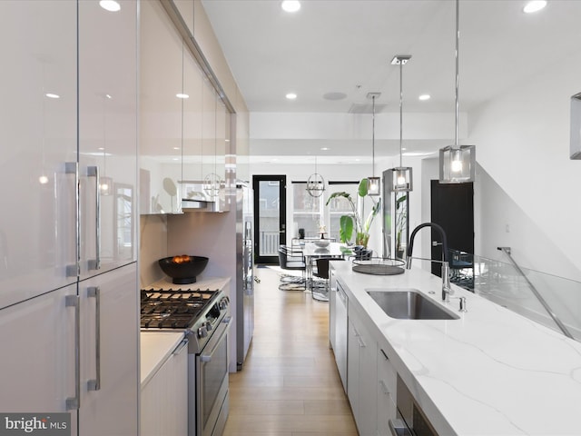 kitchen with sink, hanging light fixtures, light stone counters, stainless steel stove, and light wood-type flooring