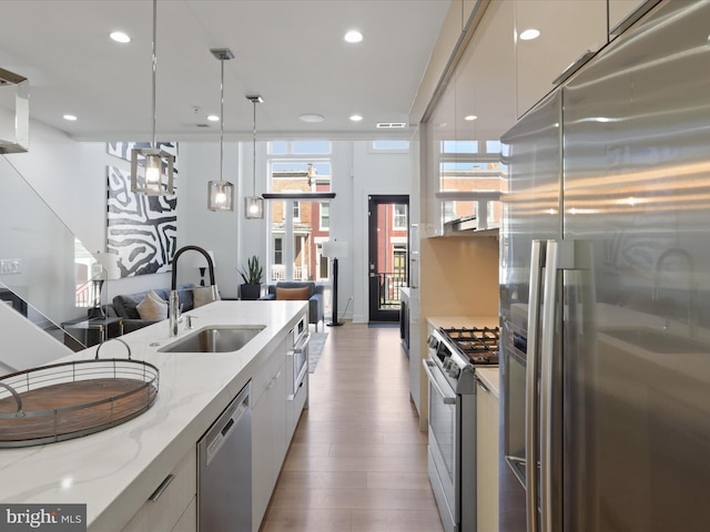 kitchen featuring hardwood / wood-style floors, sink, light stone counters, white cabinetry, and stainless steel appliances