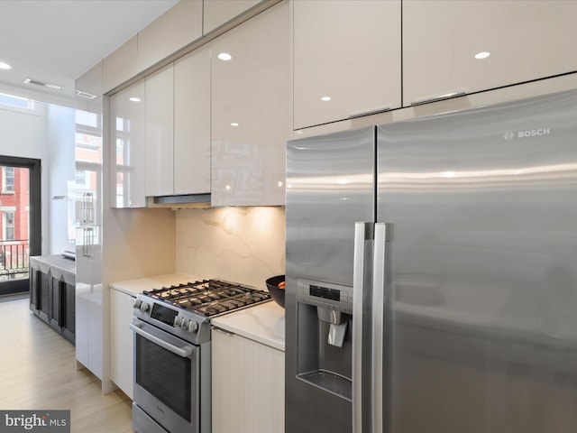 kitchen featuring decorative backsplash, white cabinets, light wood-type flooring, and high end appliances