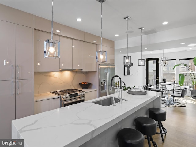 kitchen featuring a large island with sink, appliances with stainless steel finishes, hanging light fixtures, and sink