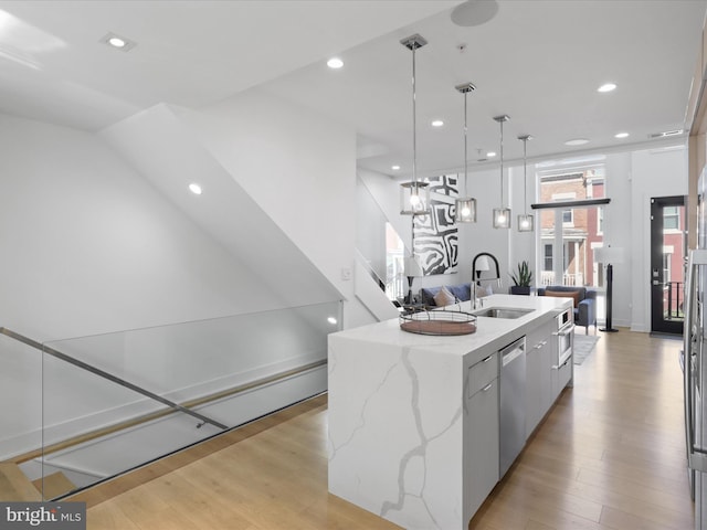 kitchen featuring a large island with sink, hanging light fixtures, sink, appliances with stainless steel finishes, and light hardwood / wood-style floors