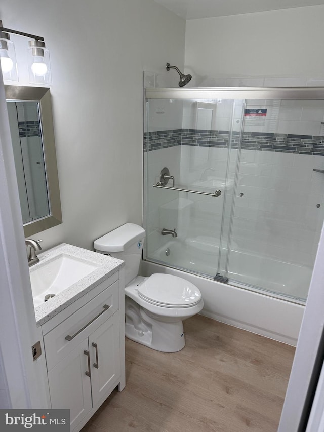 full bathroom with wood-type flooring, vanity, toilet, and bath / shower combo with glass door