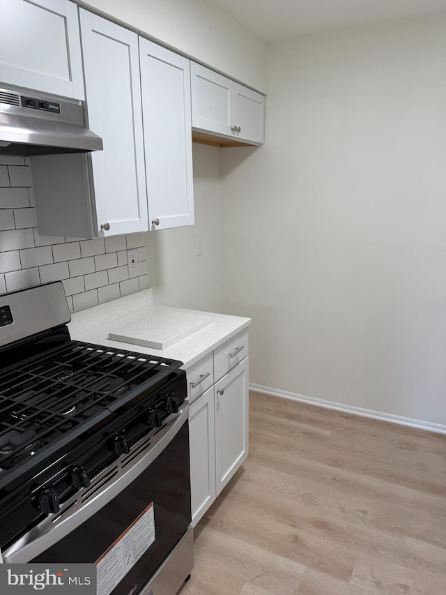 kitchen with decorative backsplash, gas stove, white cabinetry, and range hood