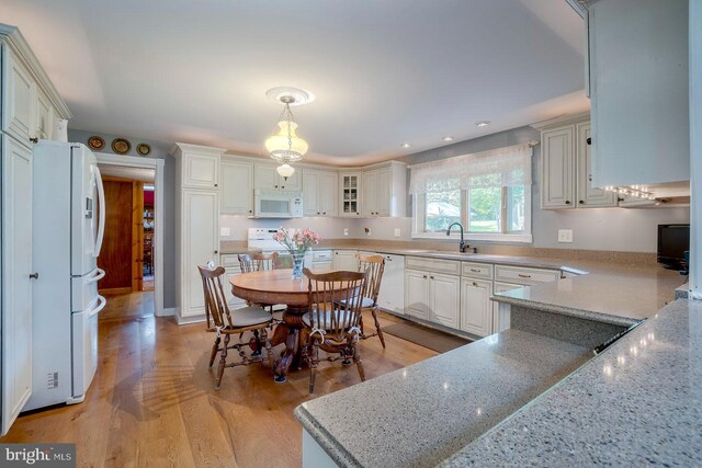 kitchen featuring white appliances, sink, decorative light fixtures, white cabinets, and light hardwood / wood-style floors