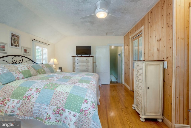 bedroom featuring ceiling fan, light hardwood / wood-style floors, a textured ceiling, lofted ceiling, and wooden walls