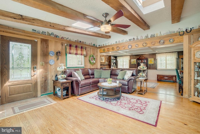 living room featuring beamed ceiling, wood-type flooring, ceiling fan, and wood walls