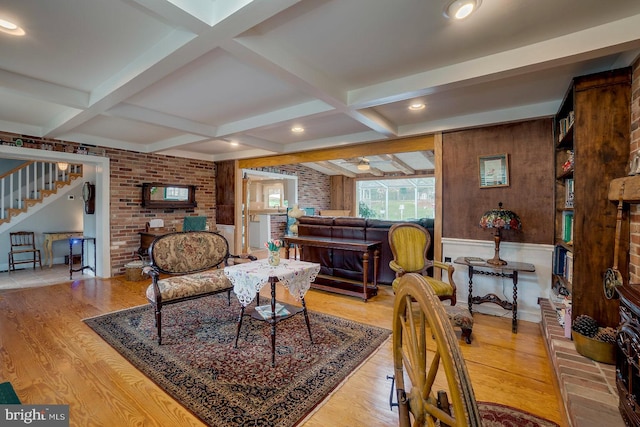 living room featuring beam ceiling, light hardwood / wood-style floors, ceiling fan, and brick wall