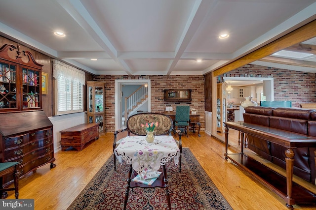 living room featuring beam ceiling, light hardwood / wood-style flooring, and brick wall