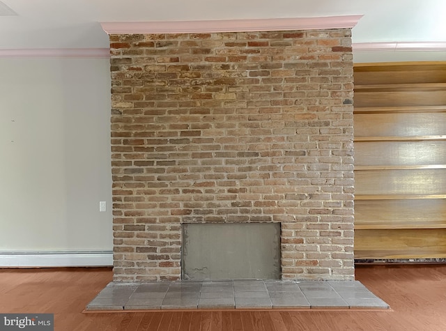 room details with wood-type flooring, a brick fireplace, ornamental molding, and a baseboard heating unit