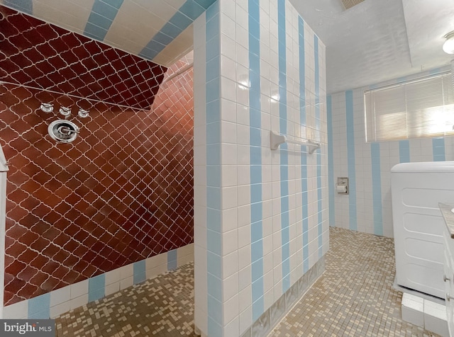 bathroom featuring tile patterned flooring, a tile shower, washer / clothes dryer, and tile walls