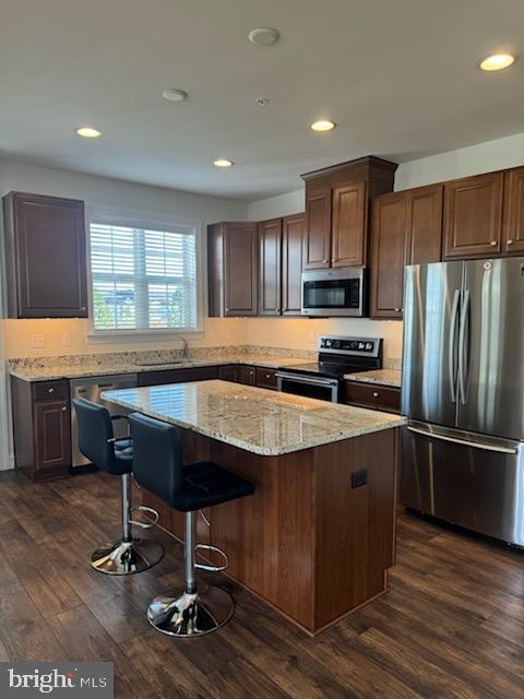 kitchen featuring a breakfast bar area, a kitchen island, dark wood-type flooring, and appliances with stainless steel finishes