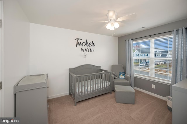 bedroom featuring ceiling fan, light colored carpet, and a crib