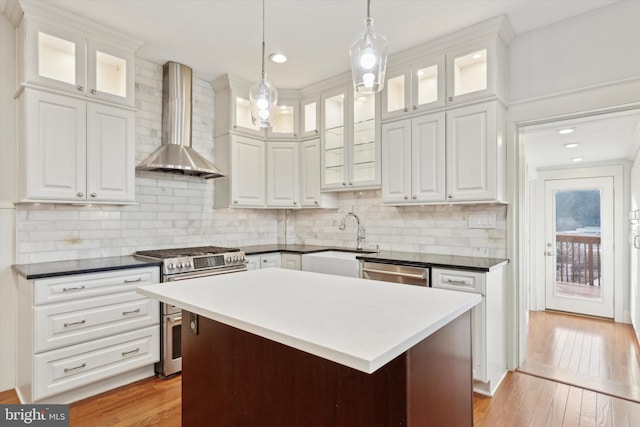 kitchen featuring white cabinets, wall chimney exhaust hood, stainless steel appliances, and decorative light fixtures