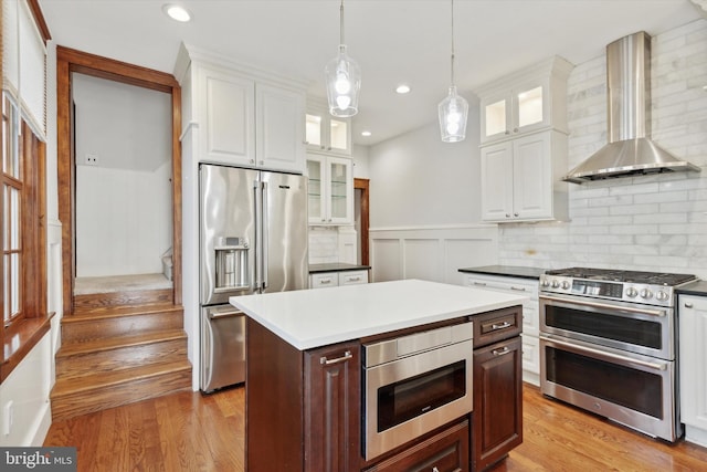 kitchen featuring pendant lighting, white cabinets, wall chimney range hood, premium appliances, and a kitchen island