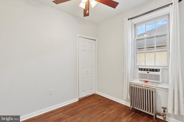 empty room with dark hardwood / wood-style floors, cooling unit, radiator heating unit, and ceiling fan