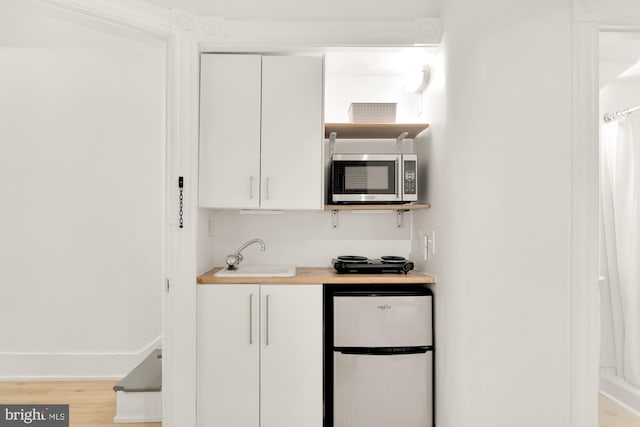 kitchen with sink, refrigerator, white cabinets, and light hardwood / wood-style floors