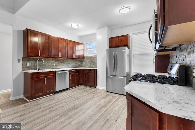 kitchen with sink, light wood-type flooring, appliances with stainless steel finishes, tasteful backsplash, and light stone counters