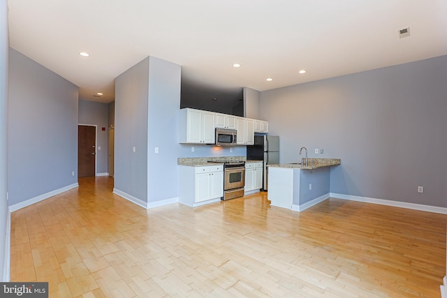 kitchen with kitchen peninsula, light hardwood / wood-style flooring, light stone countertops, white cabinetry, and stainless steel appliances