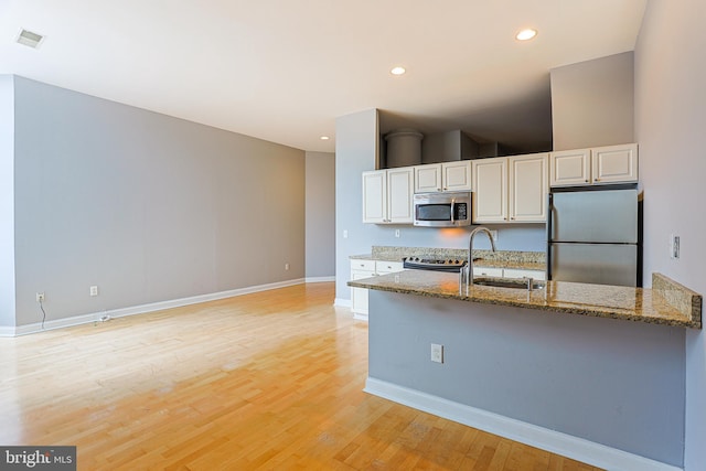 kitchen with white cabinets, stainless steel appliances, sink, stone counters, and light hardwood / wood-style floors