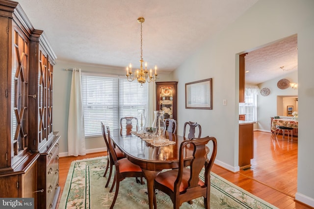 dining space featuring lofted ceiling, a notable chandelier, a textured ceiling, and light hardwood / wood-style floors