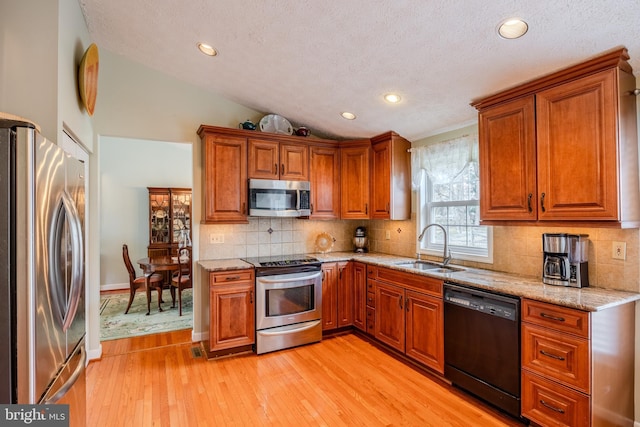 kitchen with lofted ceiling, sink, light stone counters, light hardwood / wood-style floors, and stainless steel appliances