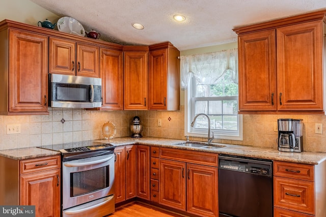 kitchen with sink, light stone counters, light wood-type flooring, stainless steel appliances, and backsplash