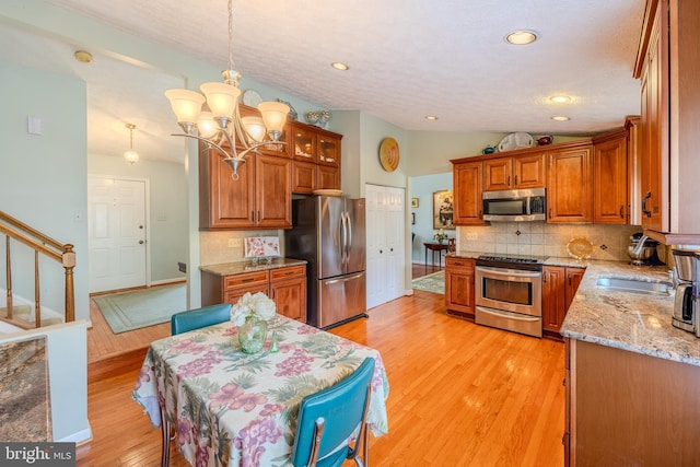 kitchen with pendant lighting, tasteful backsplash, lofted ceiling, light hardwood / wood-style floors, and stainless steel appliances