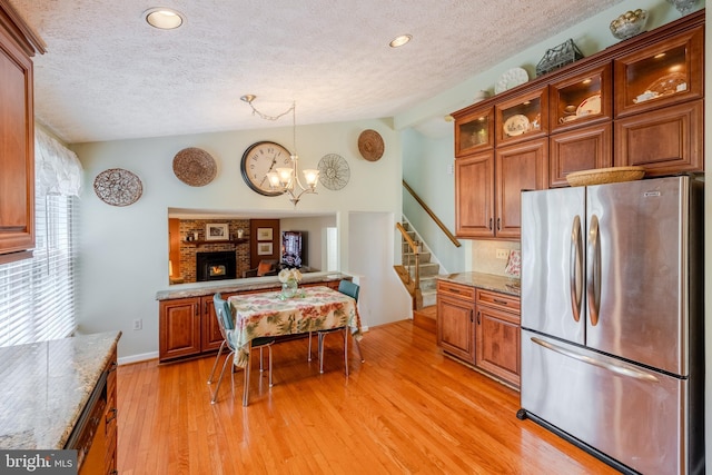 kitchen with light hardwood / wood-style flooring, stainless steel fridge, pendant lighting, a fireplace, and light stone countertops