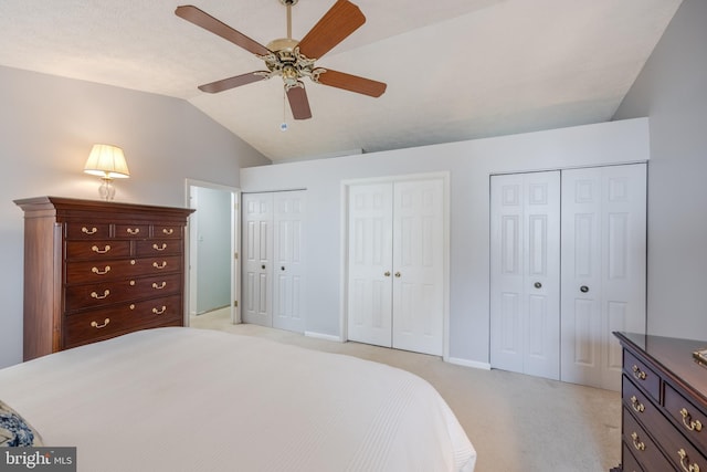 bedroom with ceiling fan, light colored carpet, lofted ceiling, and two closets