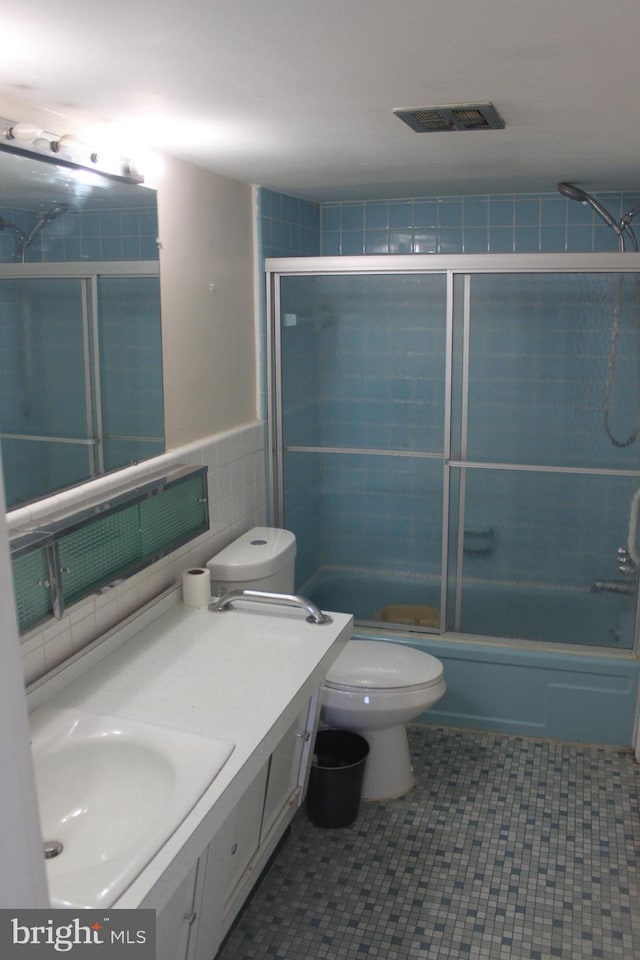 full bathroom featuring vanity, tile patterned floors, bath / shower combo with glass door, toilet, and tile walls