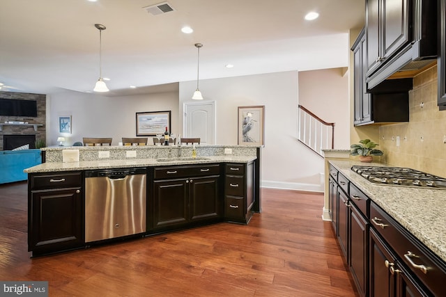 kitchen with appliances with stainless steel finishes, dark wood-type flooring, sink, pendant lighting, and a stone fireplace