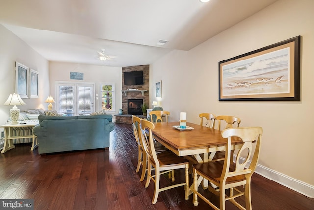 dining space with a stone fireplace, ceiling fan, and dark hardwood / wood-style floors